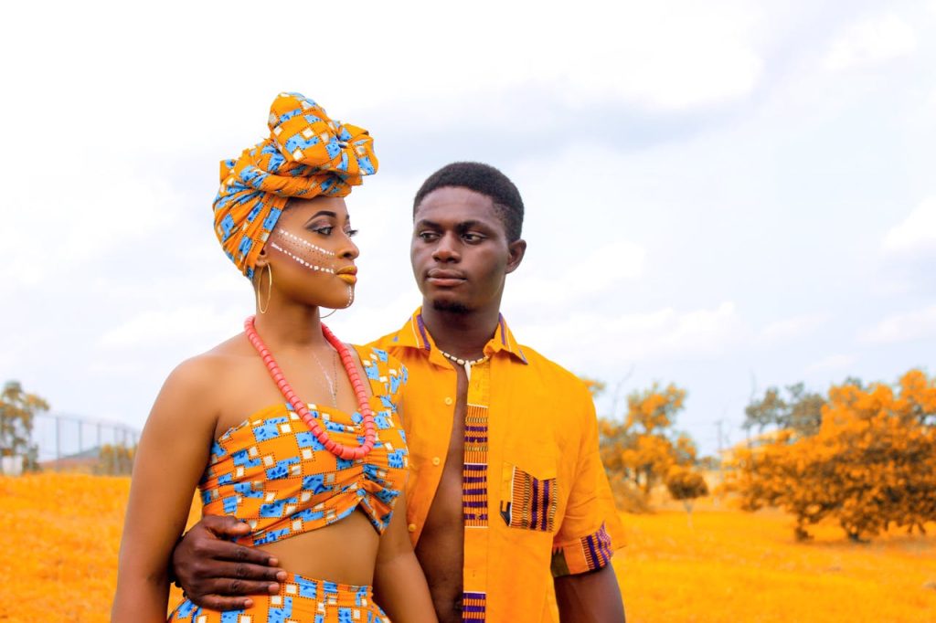A couple dressed in colorful African wear embracing outdoors in a vibrant landscape.